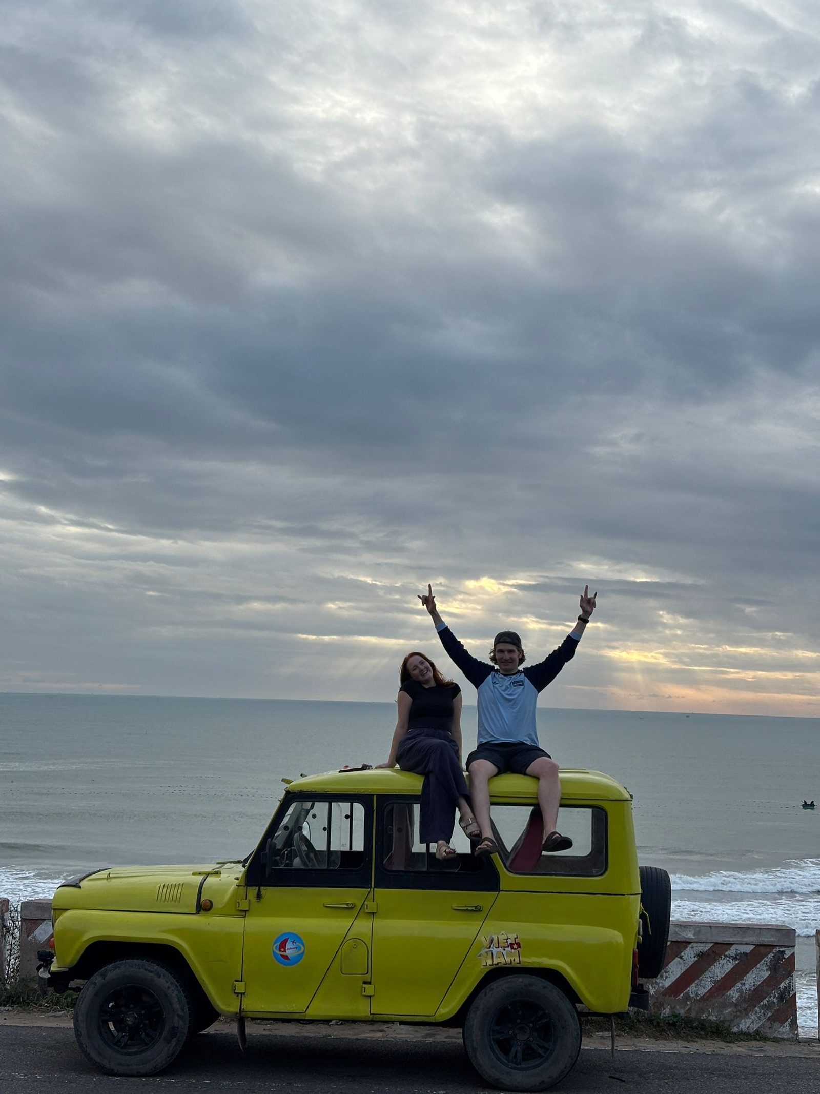 Jonty and a friend on the roof of a yellow jeep by the sea in Mui Ne, Vietnam